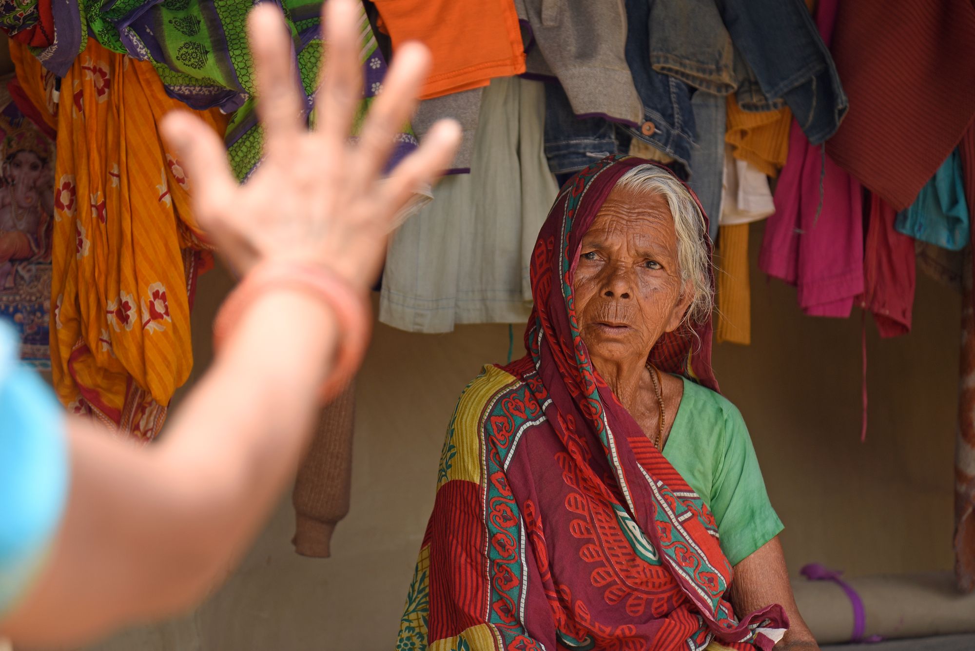An older female patient staring at a doctors hands whilst having her eyes tested. Surrounded by colourful clothing.